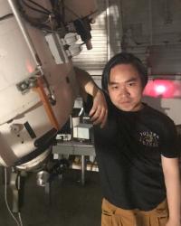Binh standing with their arm on a large telescope.