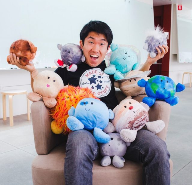 Postdoctoral scholar Michael Wong sitting with stuffed planets.