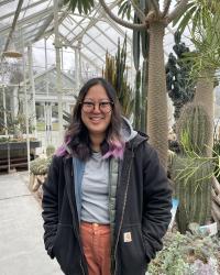 Person wearing glasses with black and purple hair standing in a desert garden