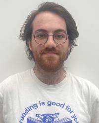 picture of white male, brown hair, glasses, bear, t-shirt that says "reading is good for you"