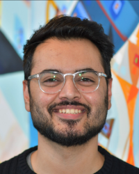 Portrait Headshot of Gourav Khullar (with glasses) in front of a blue/multicolored background.